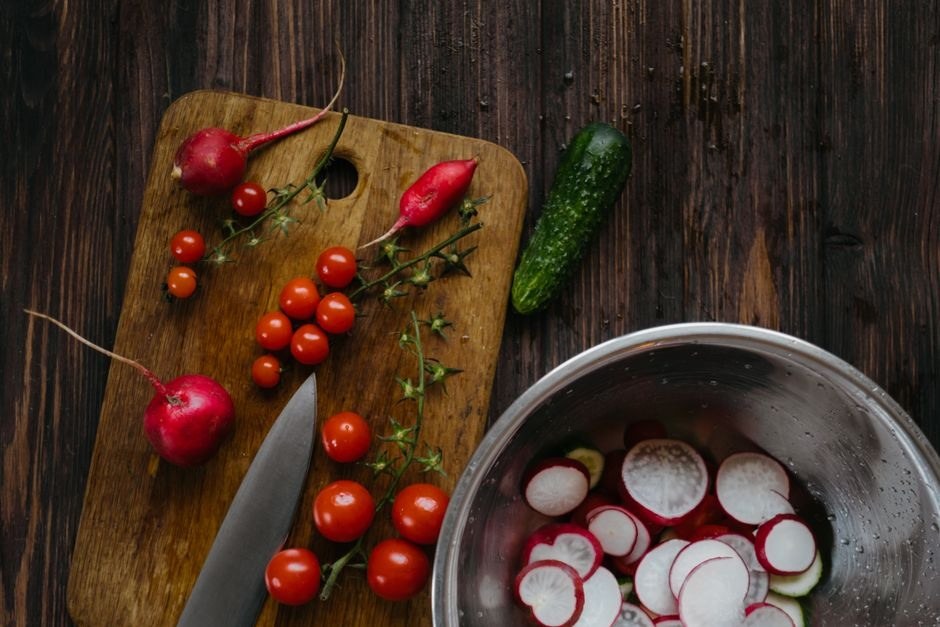 Fresh vegetables and radishes being prepared on a wooden table.
