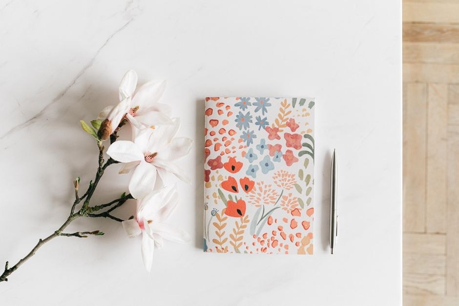 A floral notebook on a light desk beside a delicate branch.